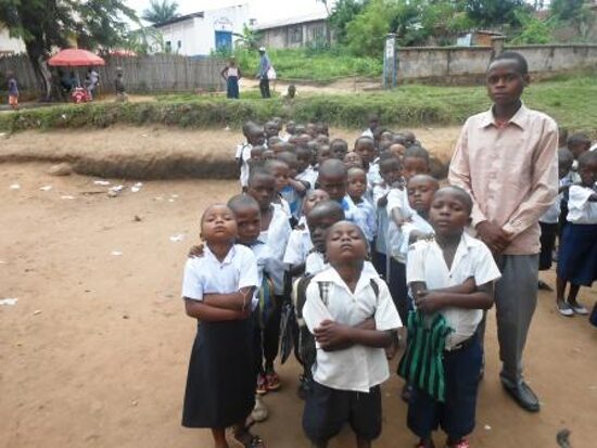 Pupils in white and blue uniforms lined up in rows in the schoolyard with their teachers