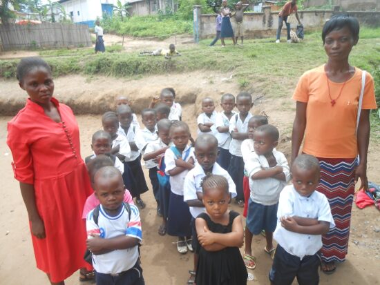 Pupils in white and blue uniforms lined up in rows in the schoolyard with their teachers