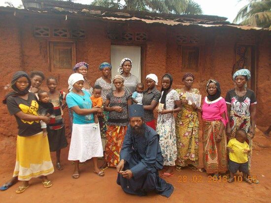 Father Theophile kneeling in front of a group of women and children of the parish