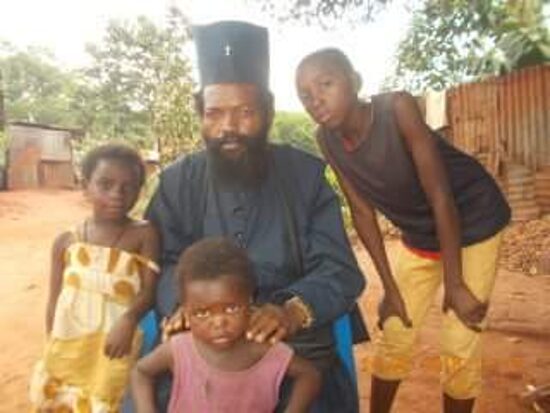 Father Theophile sitting with children of the parish