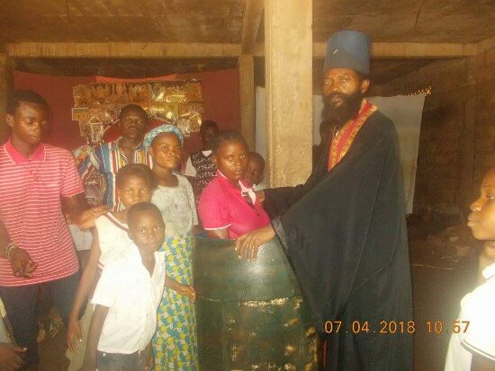 Father Theophile baptizing by immersion in a large barrel font, the faithful looking on