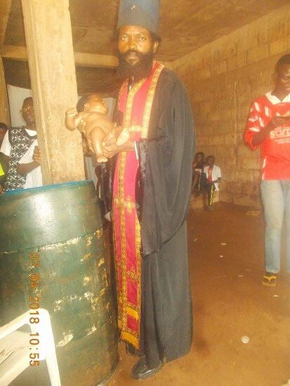 Father Theophile baptizing by immersion in a large barrel font, the faithful looking on