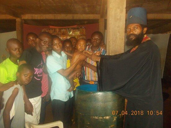 Father Theophile baptizing by immersion in a large barrel font, the faithful looking on