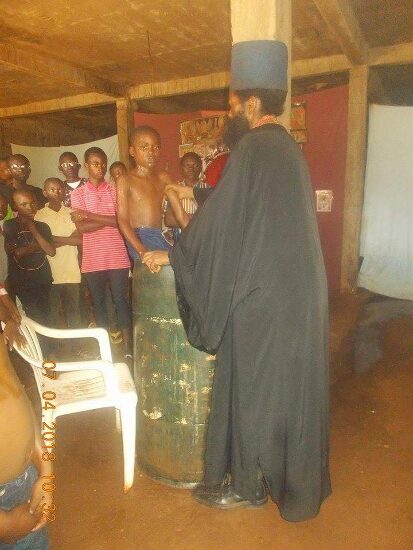 Father Theophile baptizing by immersion in a large barrel font, the faithful looking on