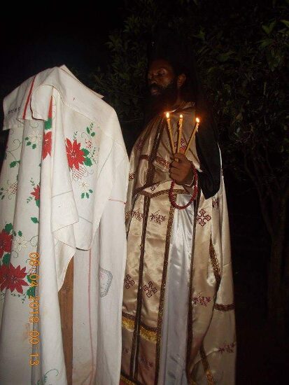 Father Theophile in vestments by night beside a lectern covered with an embroidered cloth