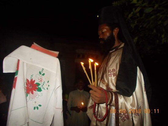 Father Theophile holding Paschal candles by a lectern covered with an embroidered cloth