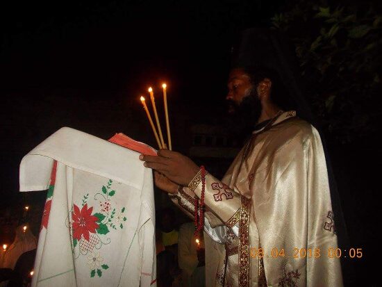 Father Theophile reading by candlelight at a lectern outside, the start of the Paschal service