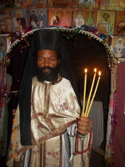 Father Theophile in vestments holding the Paschal candles in the church